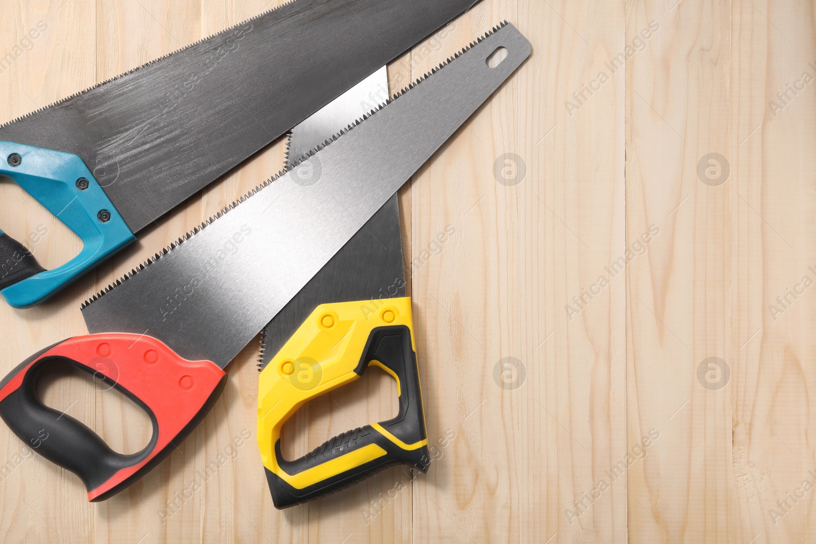 Photo of Saws with colorful handles on wooden background, flat lay. Space for text