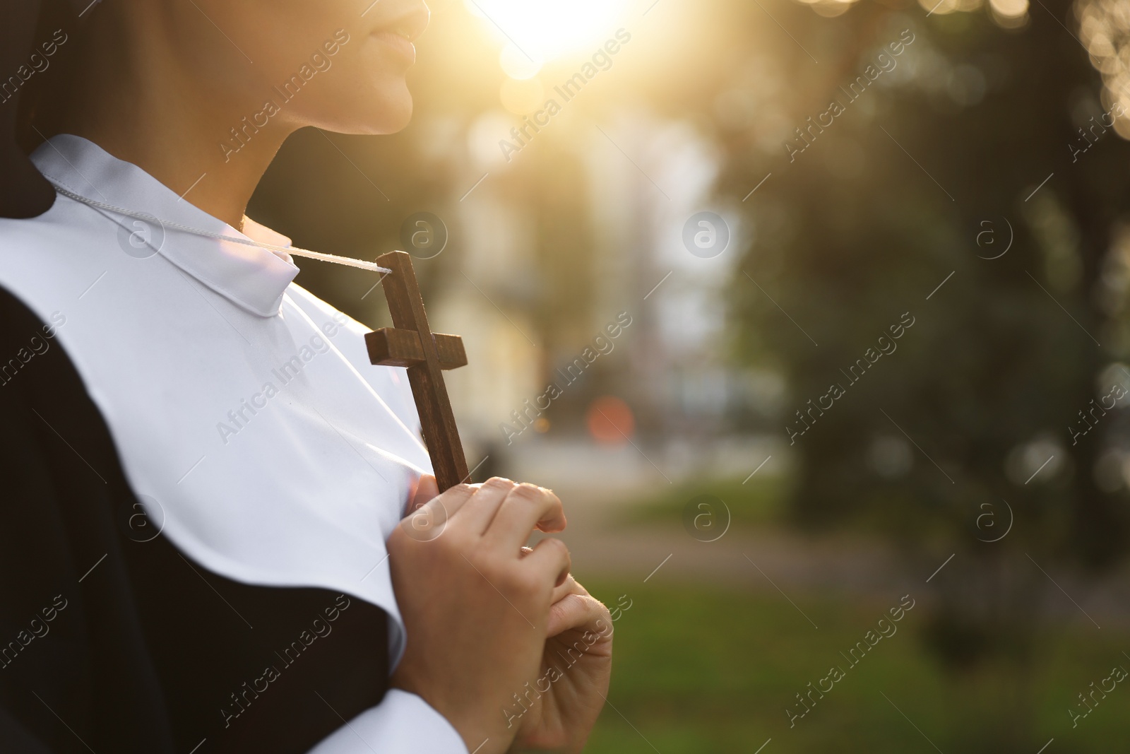 Photo of Young nun with Christian cross outdoors on sunny day, closeup. Space for text