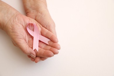 Photo of Senior woman holding pink ribbon on light background, top view with space for text. Breast cancer awareness