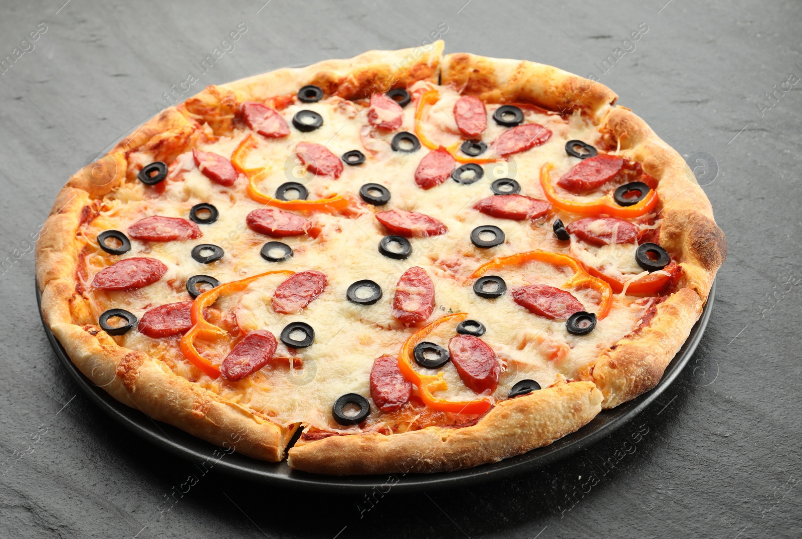 Photo of Tasty pizza with cheese, dry smoked sausages, olives and pepper on grey table