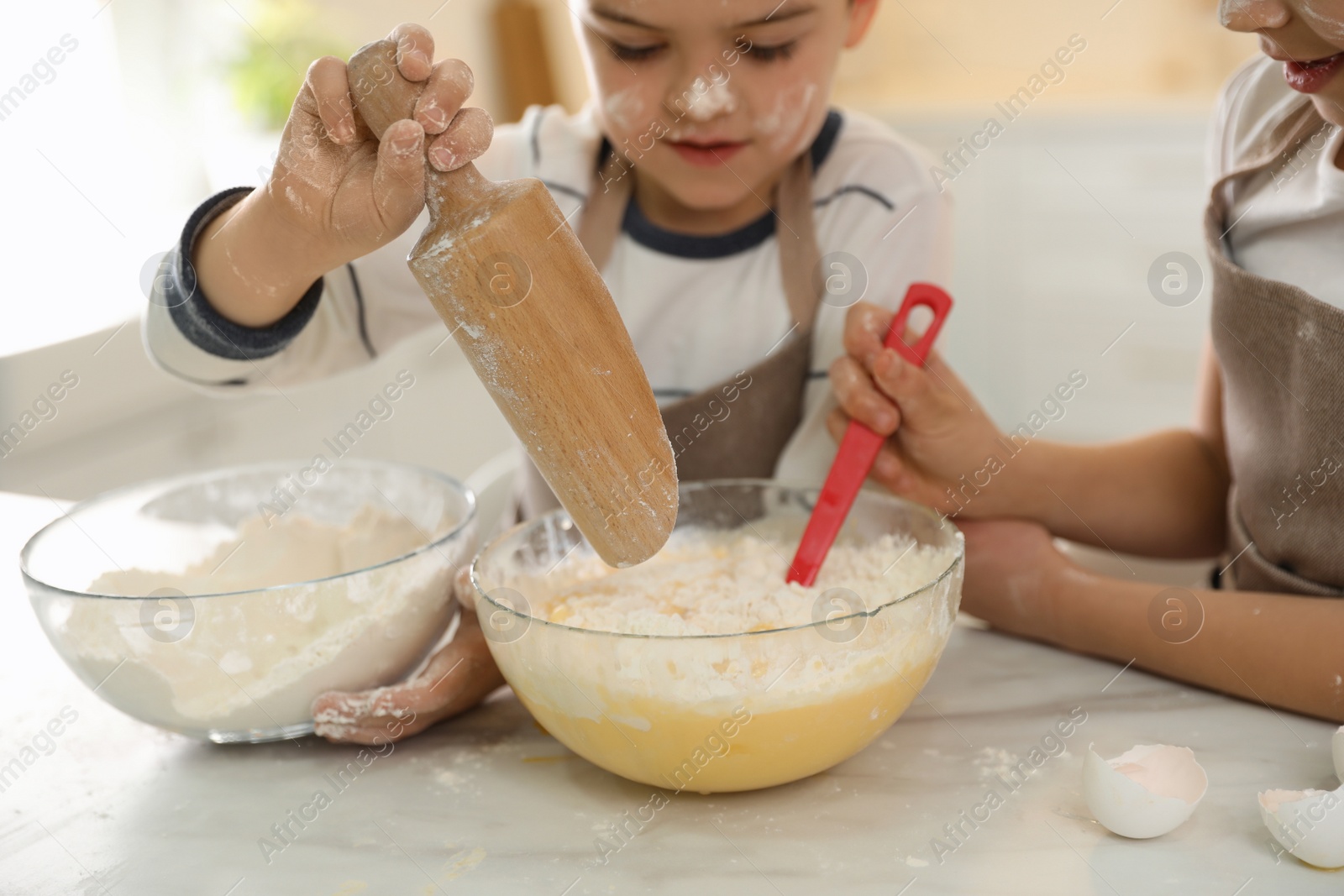 Photo of Cute little children cooking dough together in kitchen, closeup