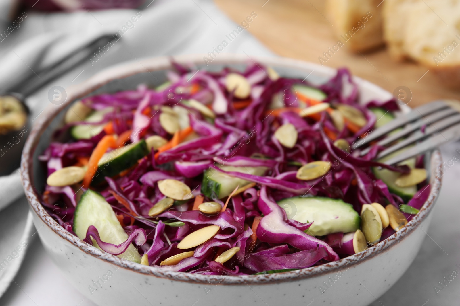 Photo of Eating tasty salad with red cabbage and pumpkin seeds on table, closeup