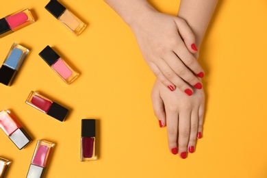 Woman with red manicure and nail polish bottles on color background, top view