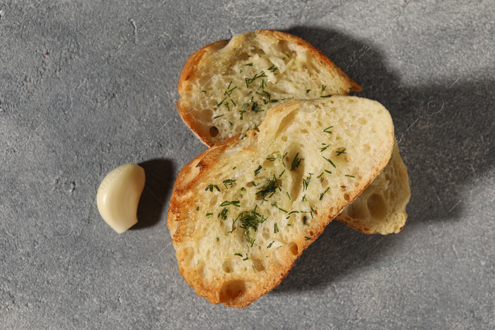 Photo of Tasty baguette with garlic and dill on grey textured table, flat lay