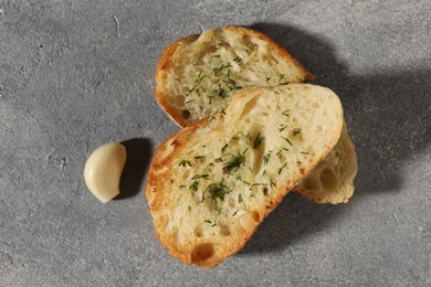Tasty baguette with garlic and dill on grey textured table, flat lay