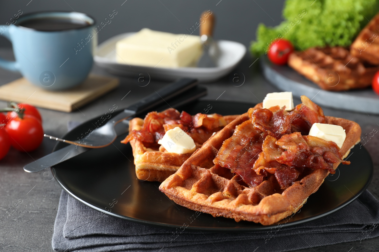 Photo of Tasty Belgian waffles served with bacon, butter and coffee on grey table, closeup