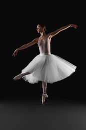 Young ballerina practicing dance moves on black background