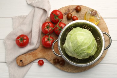 Photo of Wet cabbage in colander, oil and tomatoes on white wooden table, top view