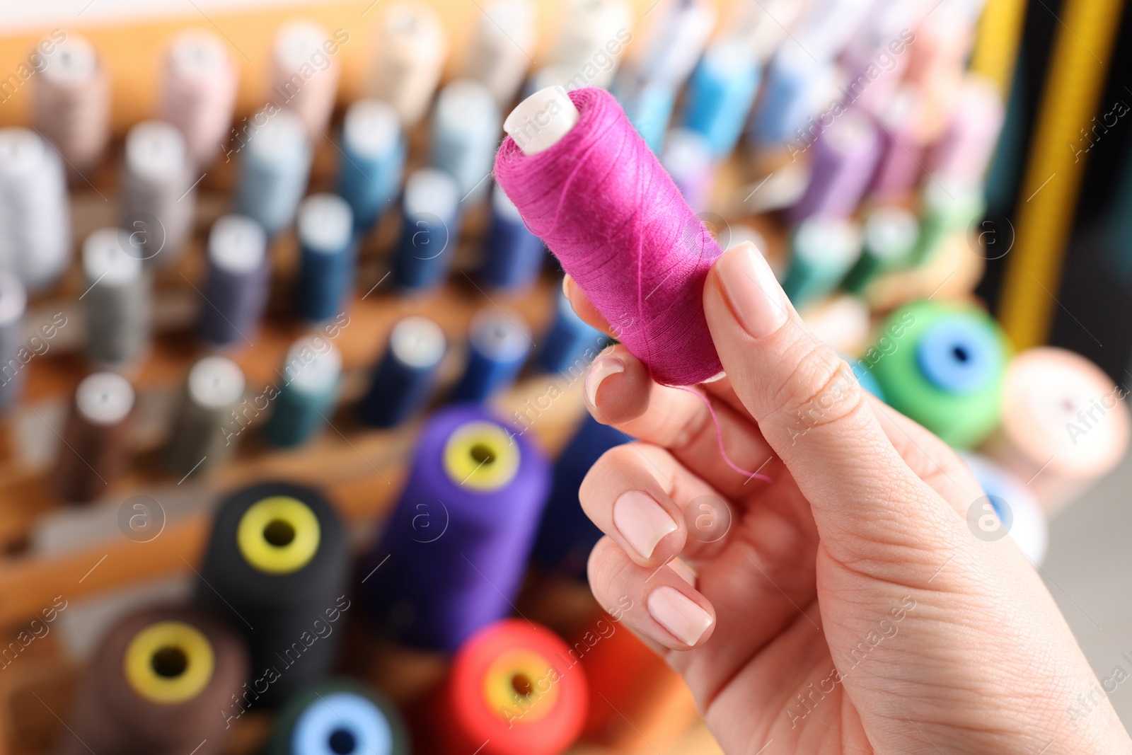 Photo of Dressmaker with pink thread near stand indoors, closeup