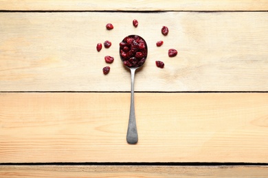 Photo of Spoon of cranberries on wooden background, top view. Dried fruit as healthy snack