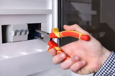 Photo of Professional repairman fixing electric panel with pliers indoors, closeup