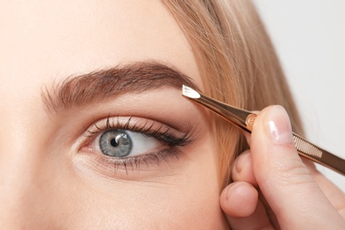 Photo of Young woman having professional eyebrow correction procedure in beauty salon