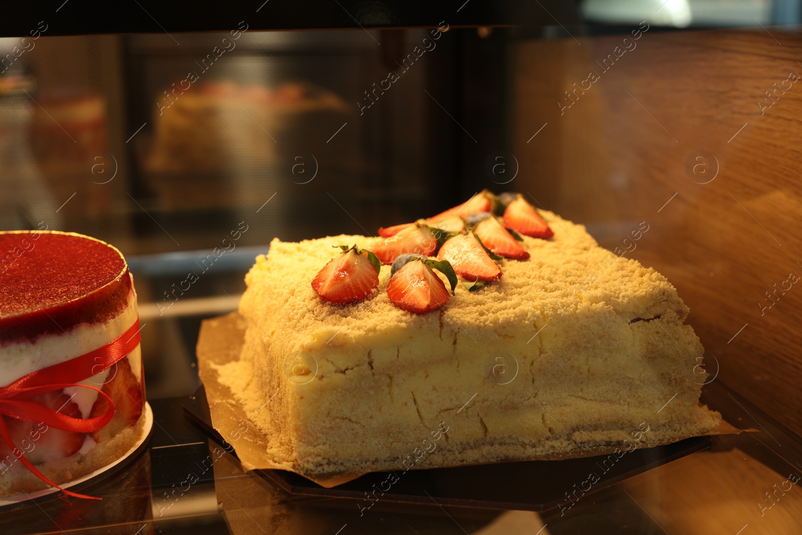 Photo of Delicious layered honey cake with fresh strawberries on counter in bakery shop, closeup