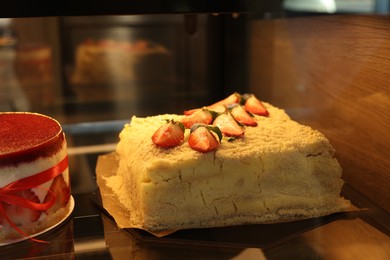 Delicious layered honey cake with fresh strawberries on counter in bakery shop, closeup