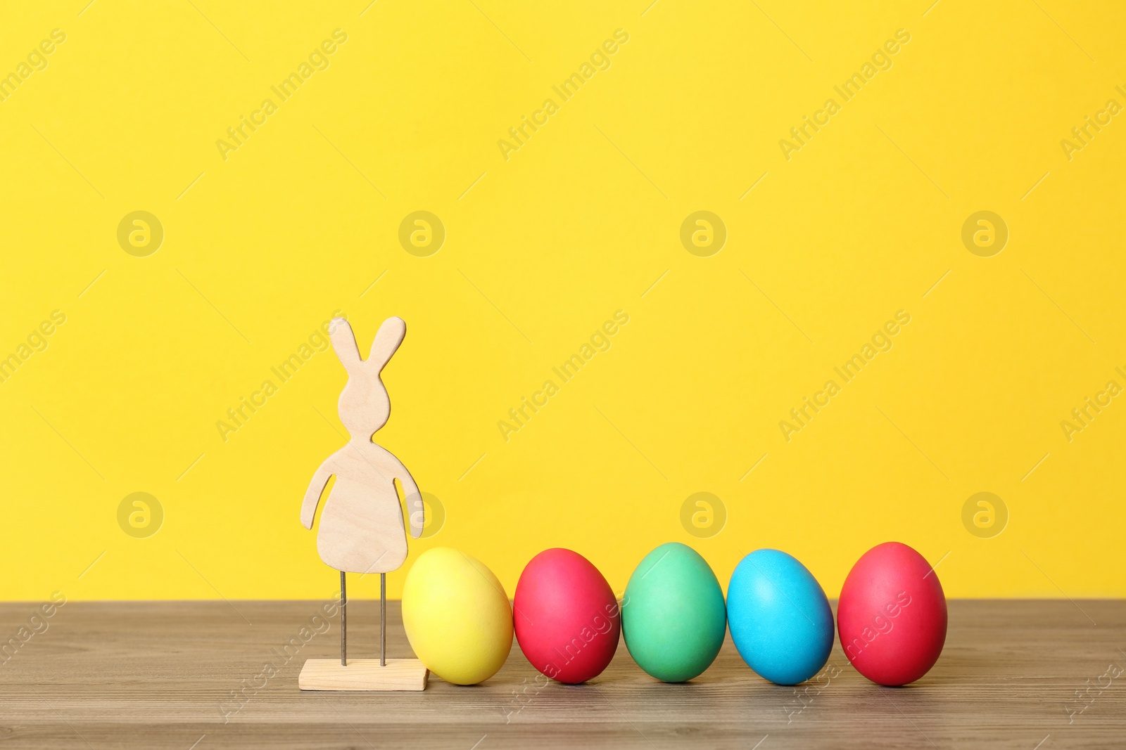 Photo of Wooden bunny and Easter eggs on table against color background