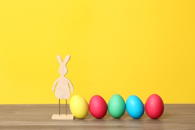 Photo of Wooden bunny and Easter eggs on table against color background