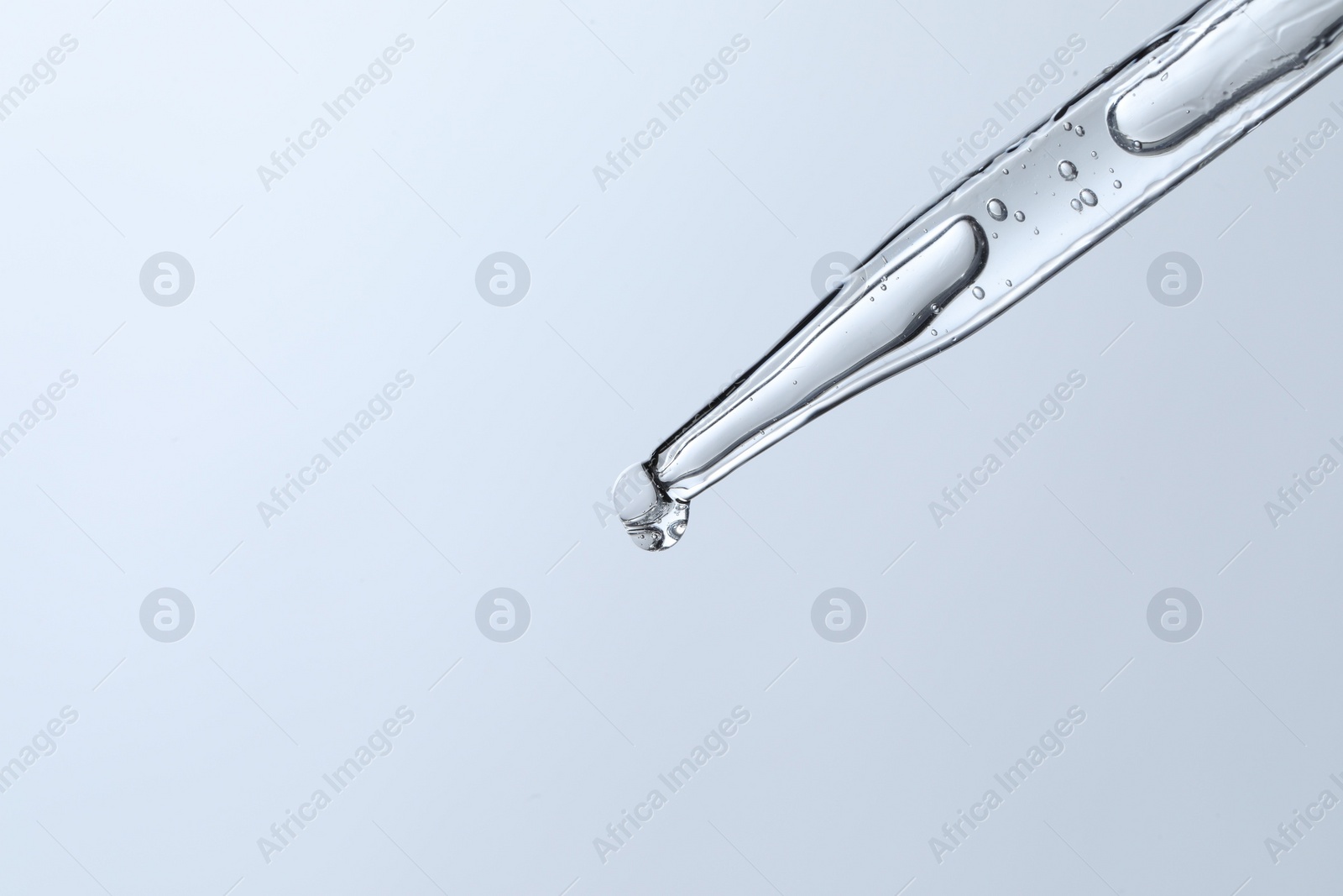 Photo of Dripping liquid from pipette on light blue background, closeup. Space for text