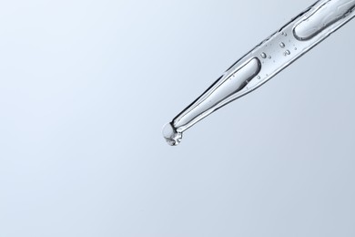 Photo of Dripping liquid from pipette on light blue background, closeup. Space for text