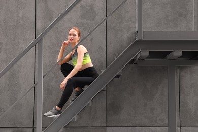 Photo of Beautiful woman in stylish gym clothes sitting on stairs on street