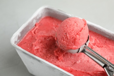 Photo of Container with delicious pink ice cream and scoop on grey table, closeup