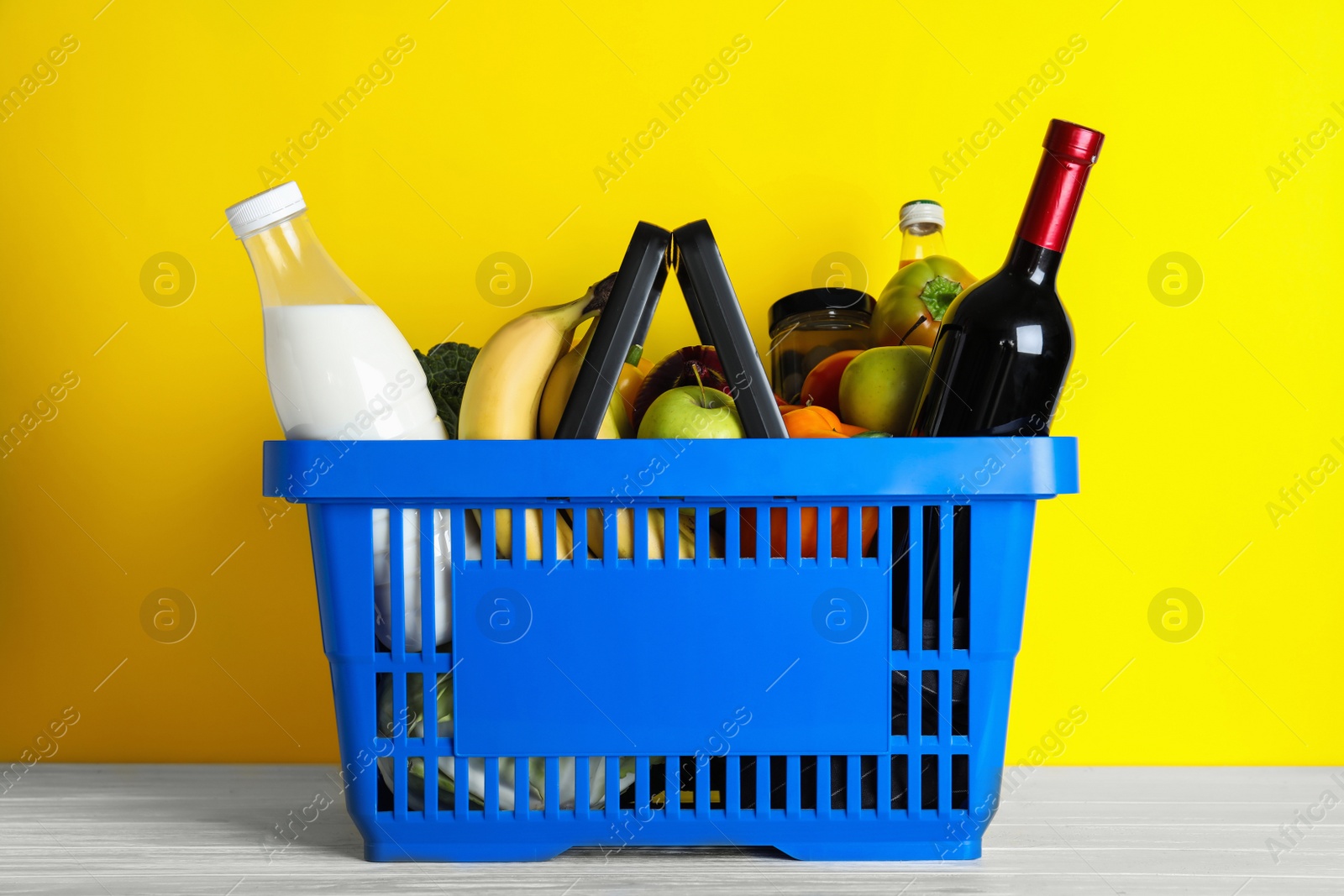 Photo of Shopping basket with grocery products on white wooden table against yellow background