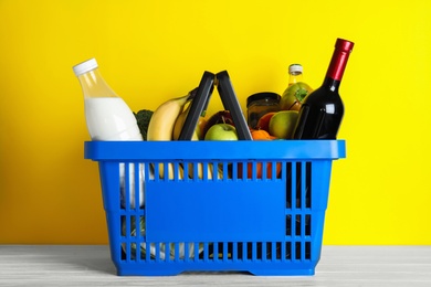 Photo of Shopping basket with grocery products on white wooden table against yellow background