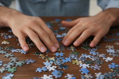 Photo of Man playing with puzzles at wooden table, closeup