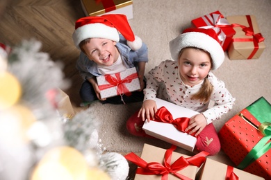 Photo of Cute little children with Christmas gifts on floor at home, above view