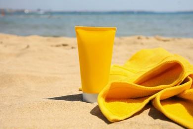 Photo of Sunscreen and towel on sandy beach, space for text. Sun protection care