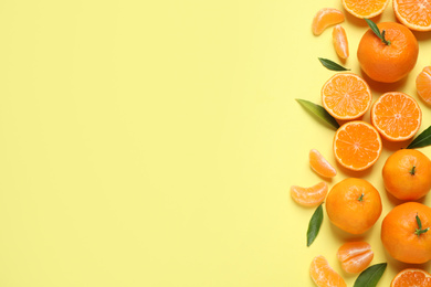 Flat lay composition with fresh ripe tangerines and leaves on light yellow background, space for text. Citrus fruit