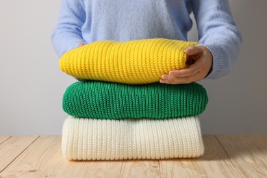 Woman with folded sweaters at wooden table on light background, closeup