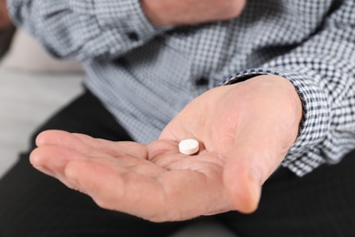 Senior man holding pill in hand, closeup