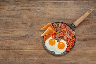Photo of Serving pan of fried eggs, mushrooms, beans, bacon, tomatoes and toasted bread on wooden table, top view with space for text. Traditional English breakfast