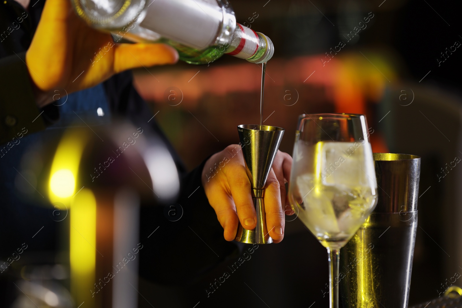 Photo of Cocktail making. Bartender pouring alcohol from bottle into jigger on blurred background, closeup