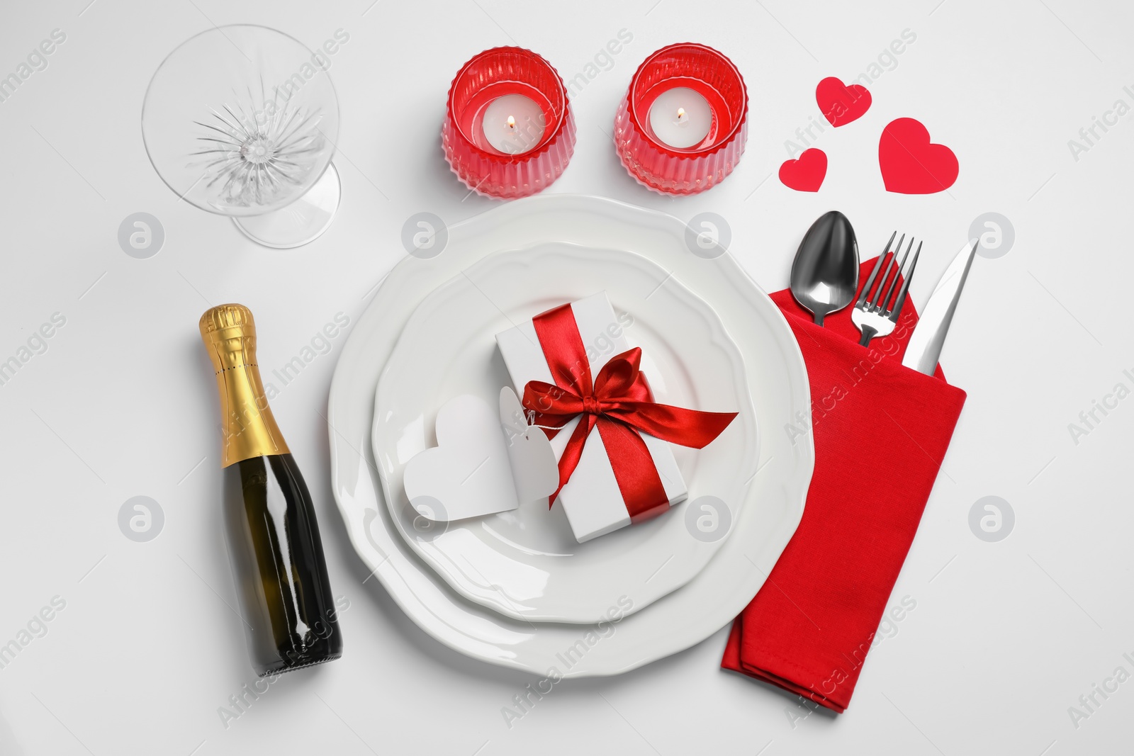 Photo of Beautiful table setting with burning candles, gift box and sparkling wine for romantic dinner on white background, flat lay