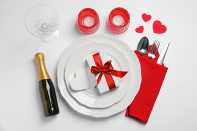 Photo of Beautiful table setting with burning candles, gift box and sparkling wine for romantic dinner on white background, flat lay