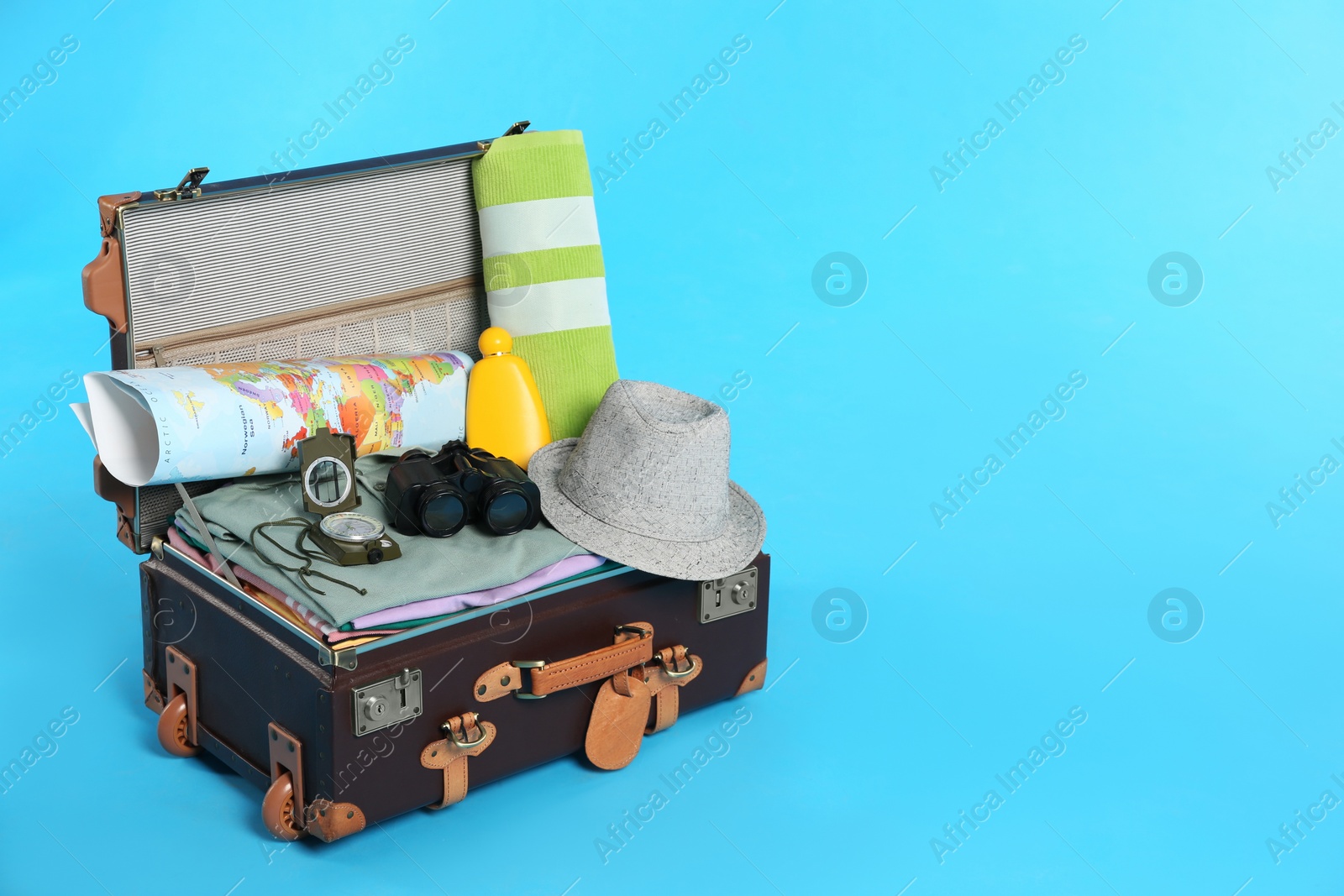 Photo of Packed vintage suitcase with clothes on light blue background, space for text. Summer vacation