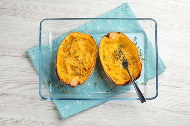 Photo of Halves of cooked spaghetti squash with thyme and fork in baking dish on white wooden table, top view