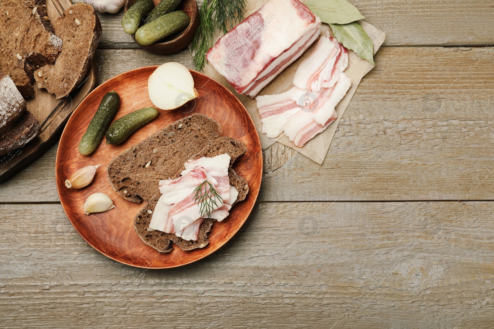 Photo of Tasty salt pork with rye bread, pickled cucumbers and dill on wooden table, flat lay. Space for text