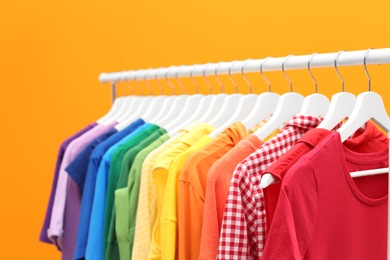 Rack with rainbow clothes on color background