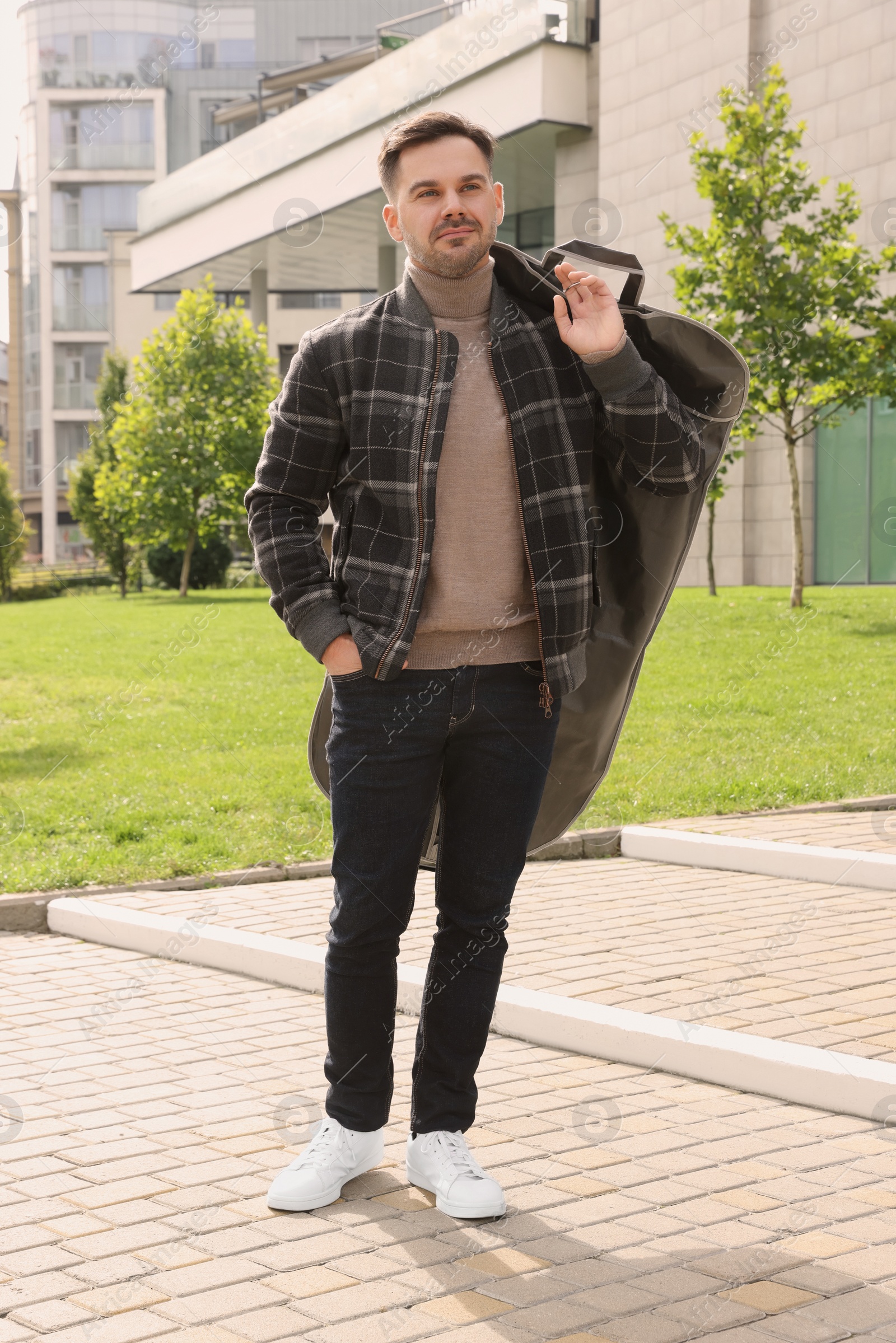 Photo of Man holding garment cover with clothes outdoors. Dry-cleaning service