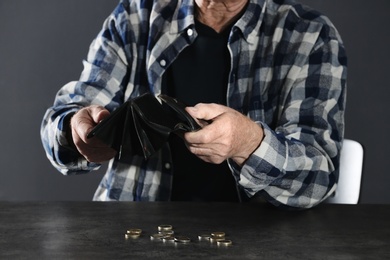 Poor elderly man with empty wallet and coins at table, closeup