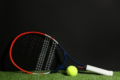 Tennis racket and ball on green grass against black background. Space for text