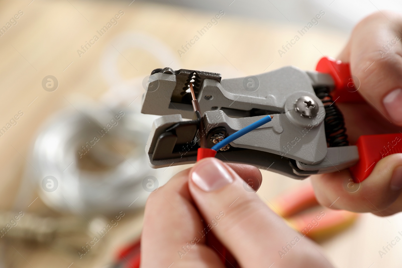 Photo of Professional electrician stripping wiring against blurred background, closeup view