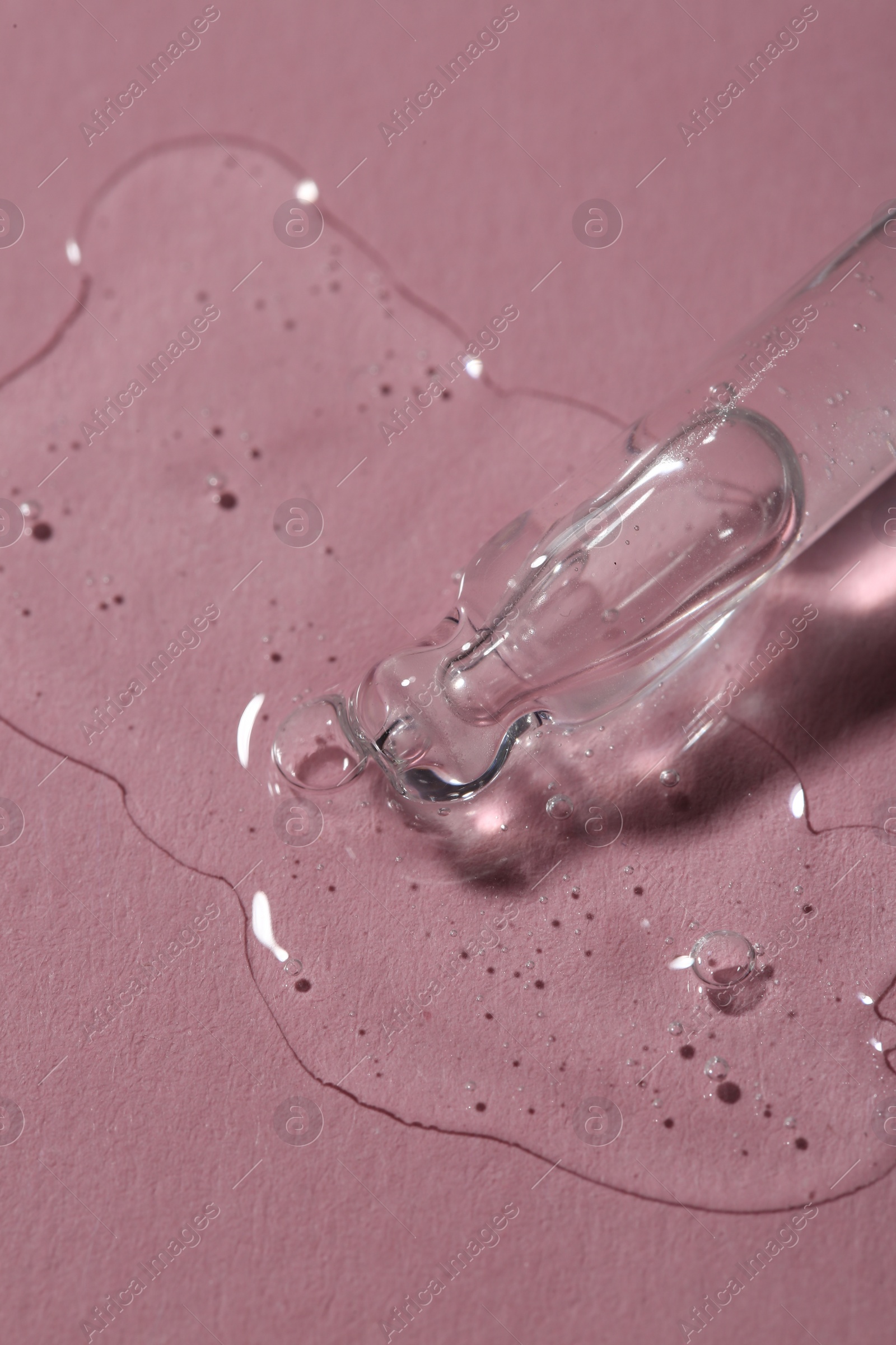 Photo of Dripping cosmetic serum from pipette onto pink background, macro view