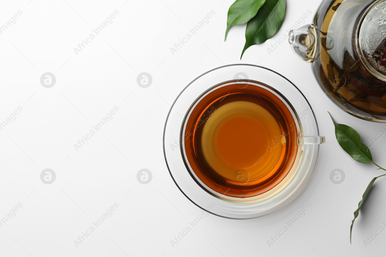 Photo of Fresh green tea in glass cup with saucer and leaves on white table, flat lay. Space for text