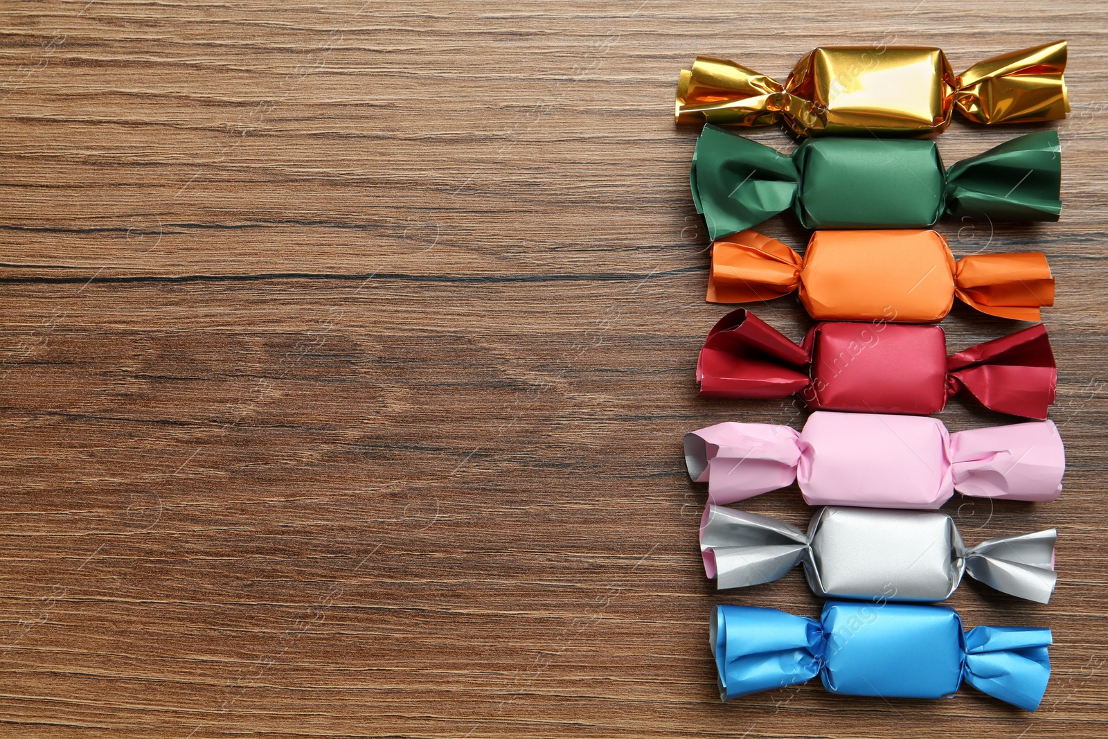 Photo of Many candies in colorful wrappers on wooden table, flat lay. Space for text