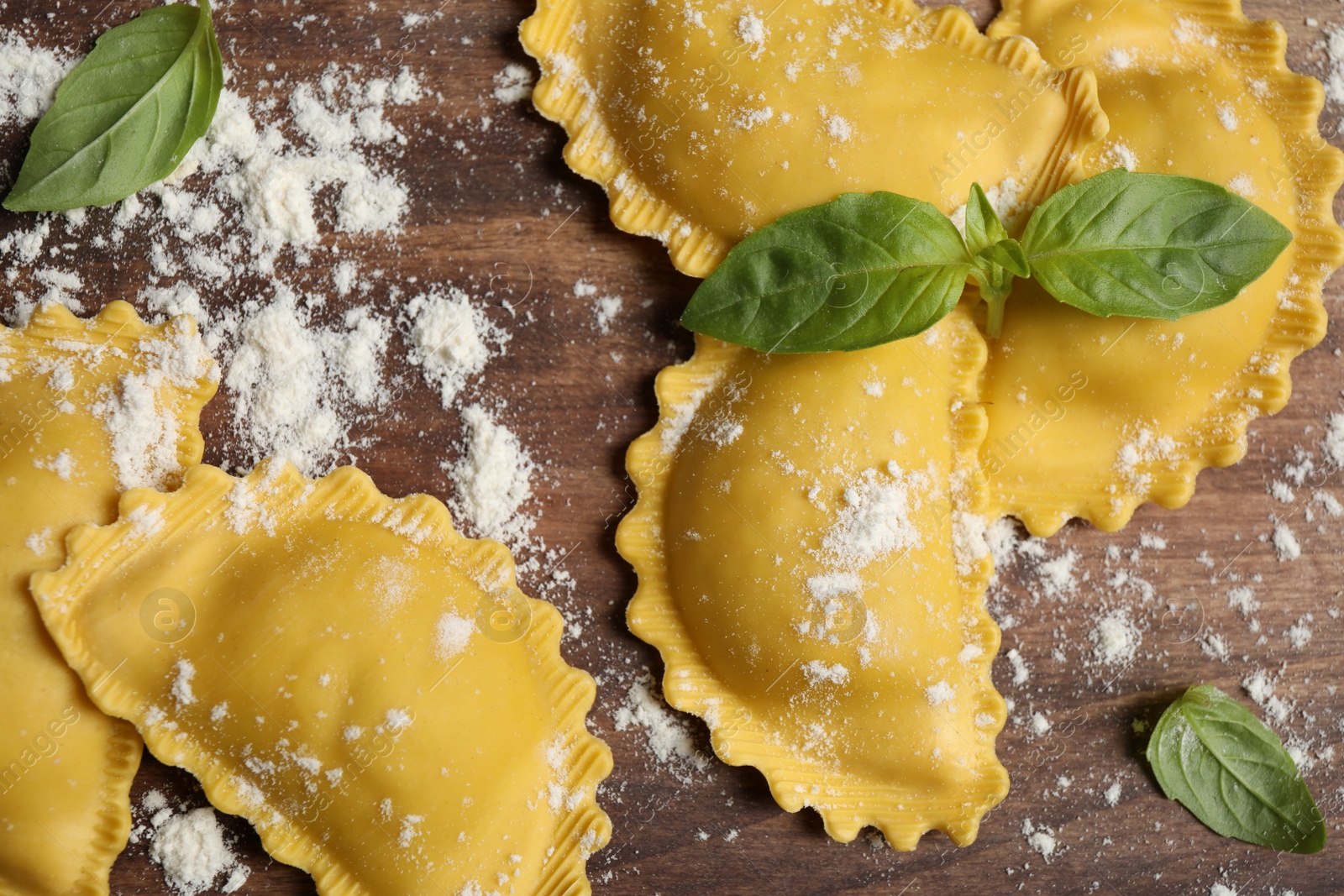 Photo of Raw ravioli with basil on wooden table, flat lay. Italian pasta