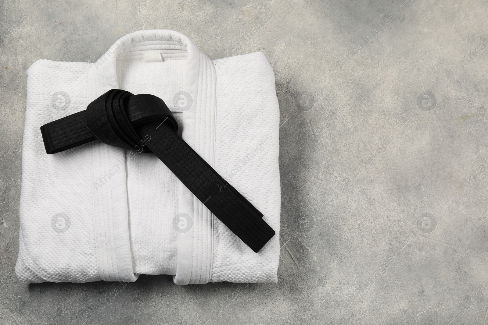 Photo of Black karate belt and white kimono on gray textured background, top view. Space for text