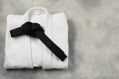 Photo of Black karate belt and white kimono on gray textured background, top view. Space for text